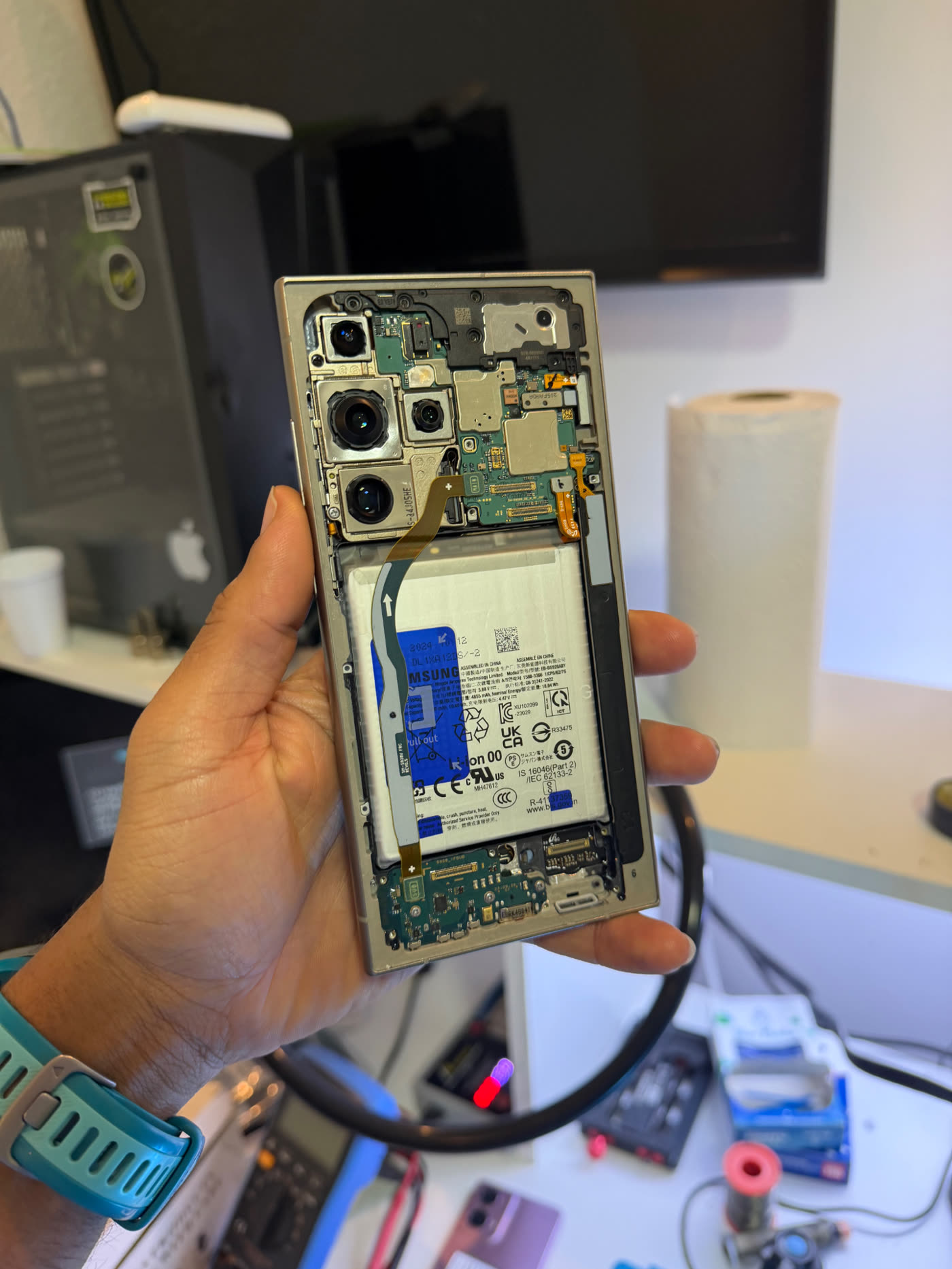 Técnico da TECHCEL com smartphone aberto na bancada, exibindo placa e bateria